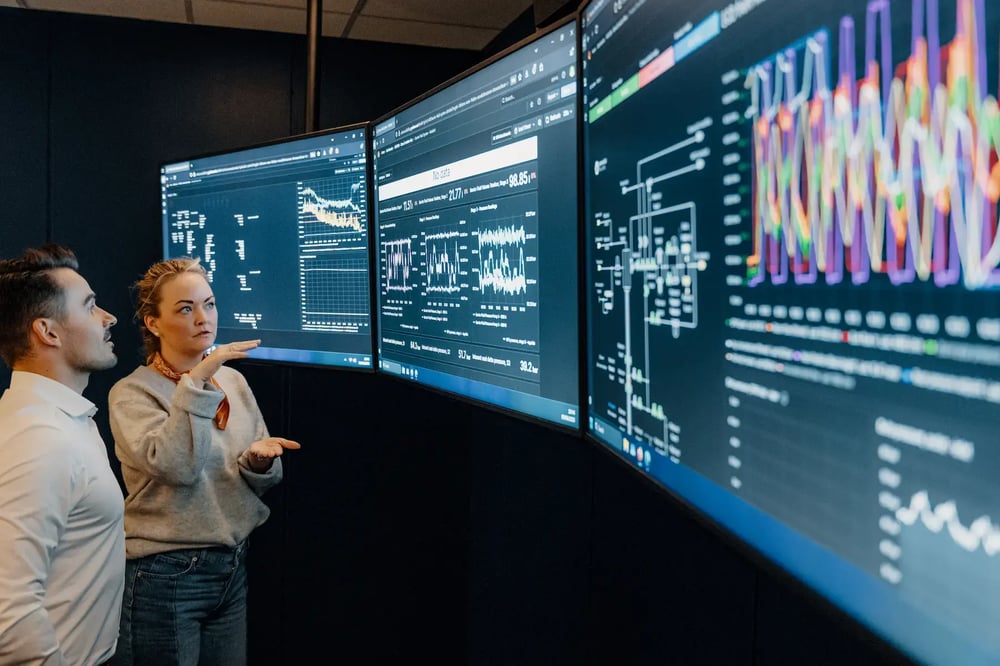 Two engineers at Enhanced Drilling analyzing real-time well data on multiple monitoring screens. Two engineers at Enhanced Drilling analyzing real-time well data on multiple monitoring screens.