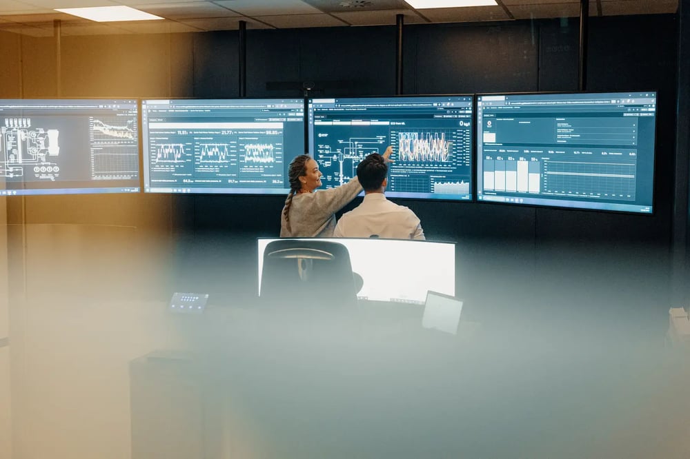 Two engineers at Enhanced Drilling monitoring well performance data across multiple large screens. Two engineers at Enhanced Drilling monitoring well performance data across multiple large screens.