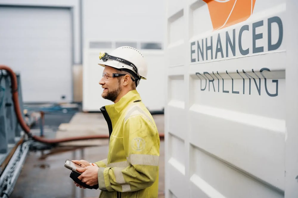 Enhanced Drilling engineer in safety gear holding a device outside the workshop. Enhanced Drilling engineer in safety gear holding a device outside the workshop.