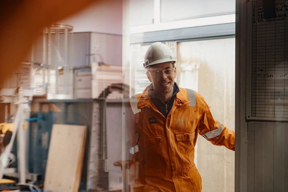 Enhanced Drilling engineer in orange coveralls entering a workshop with a smile. Enhanced Drilling engineer in orange coveralls entering a workshop with a smile.